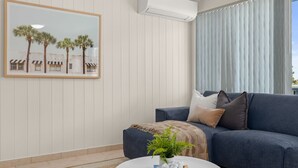 Una sala de estar con un sofá azul, un cuadro con palmeras y una planta en una mesa redonda.