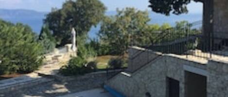 Área de piscina com estrutura de pedra, cercada por vegetação e vista para o mar.