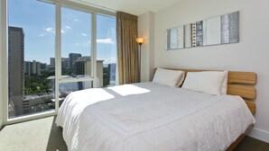 Ein Hotelzimmer mit großem Fenster, einem Bett mit weißer Bettwäsche, einem Holz-Kopfende und einem an der Wand hängenden Kunstwerk.