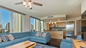Ein modernes Wohnzimmer mit einem Ecksofa, einem Holztisch und Blick auf die Stadt durch große Fenster.