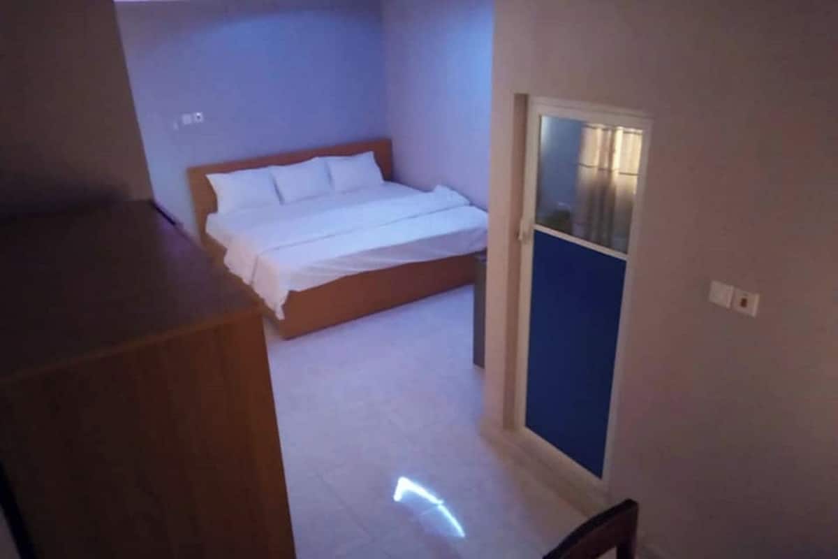 Une chambre à coucher avec un lit, une table de chevet en bois et une porte donnant sur une autre pièce.