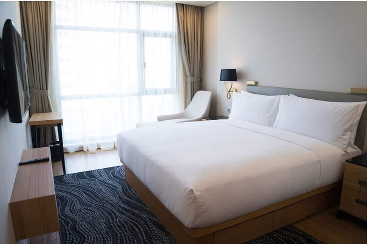 Une chambre d’hôtel avec un grand lit, un bureau, une chaise, une télévision et une fenêtre avec des rideaux.