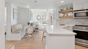 Een moderne keuken met witte kastjes, een centraal eiland en een eethoek met rieten stoelen.