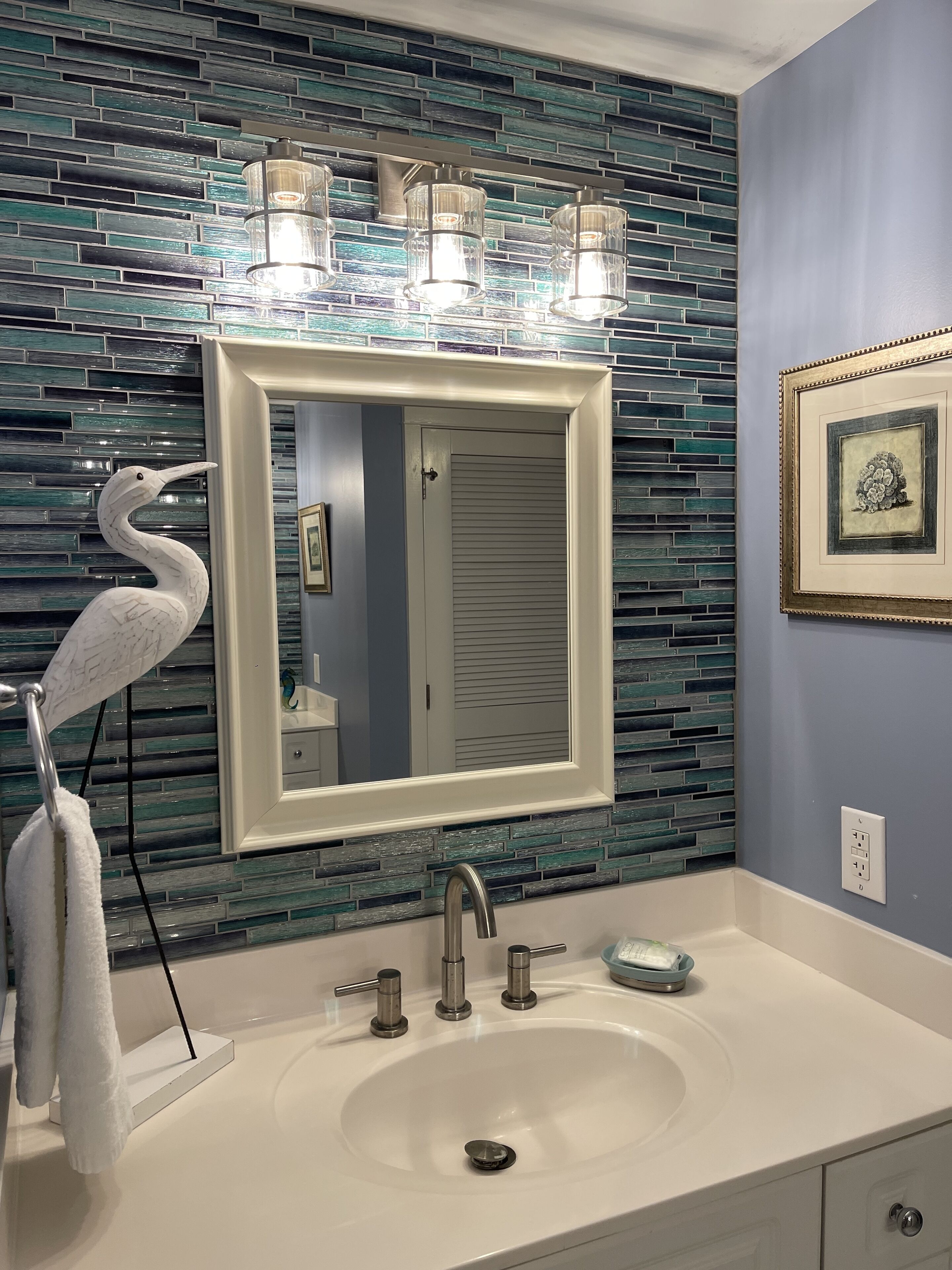Un baño con un lavamanos blanco, un espejo y una pared con mosaicos azules y verdes.