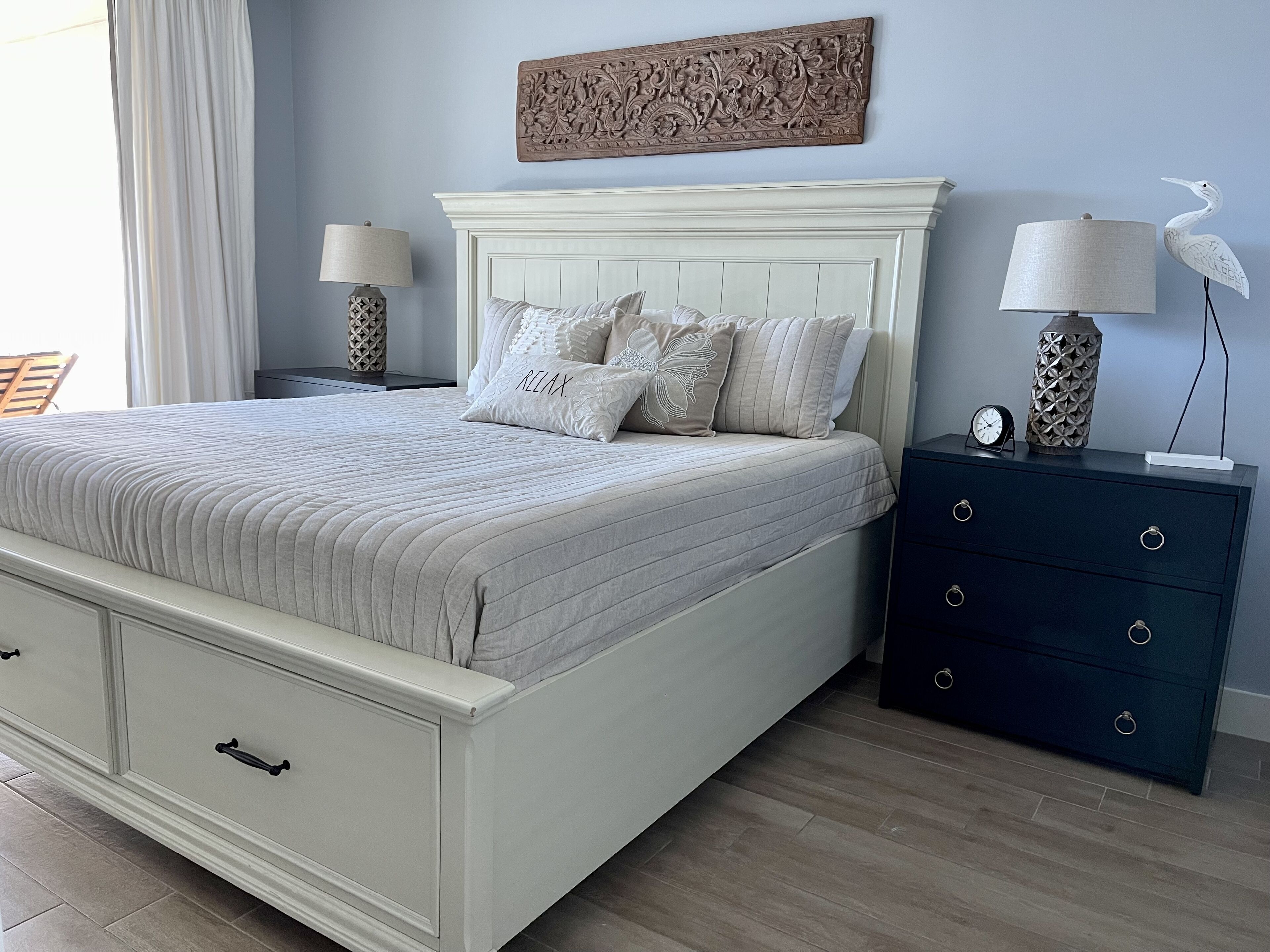 A bedroom with a bed, nightstands, a dresser, and a wall-mounted artwork.