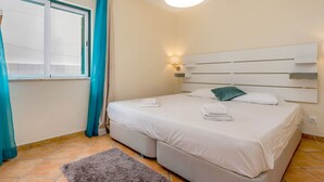 A bedroom with a bed, a window with curtains, a wall-mounted light, and a rug. - Villa som das Ondas I (Budens)