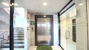 Ascensor en un edificio moderno con un felpudo verde en la entrada, un botón pulsador y un letrero que indica acceso limitado.