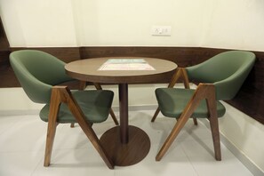 A round wooden table with a menu in the center, surrounded by two green upholstered chairs with wooden legs.