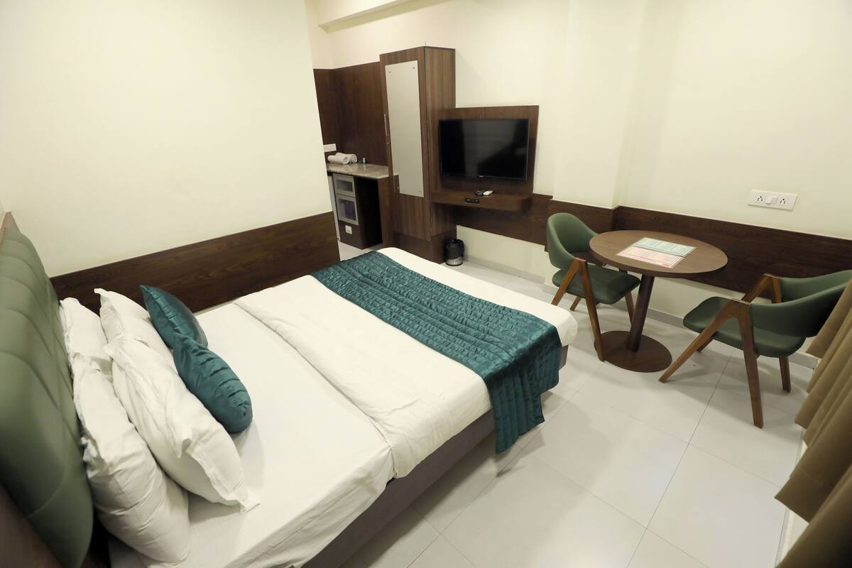 A hotel room with a bed, a desk, a television, and two chairs.