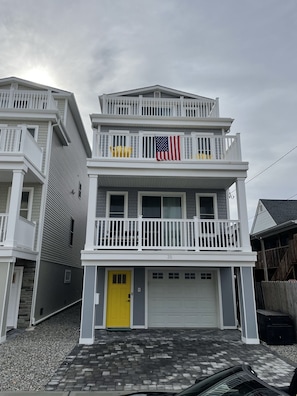 A two-story building with a yellow front door, a garage, and a balcony with an American flag.