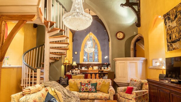 A cozy living room with a staircase, a chandelier, and a stained glass window.