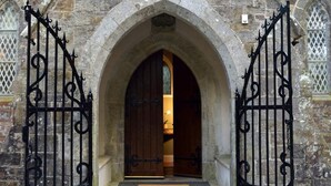 A stone building with a large arched entrance, a wooden door, and black wrought iron gates.