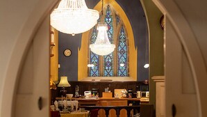 A cozy living room with a fireplace, a chandelier, and a view of a kitchen through a stained glass window.