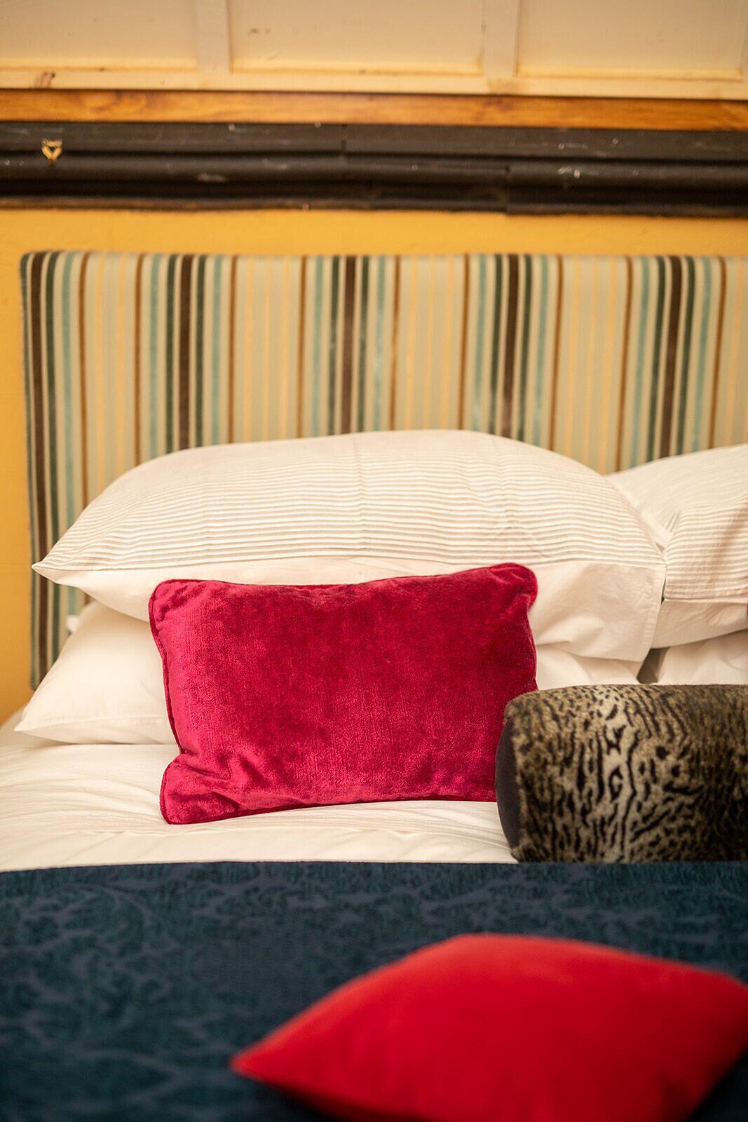 A bed with striped headboard, white pillows, and a red pillow.