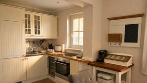 Una cocina con muebles blancos, horno empotrado, cafetera y una ventana que proporciona luz natural.
