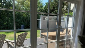 Una habitación con ventanas amplias, mobiliario de mimbre y vistas a un jardín.