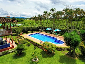 Una piscina rodeada de abundante vegetación, un pabellón y vistas a montañas distantes.