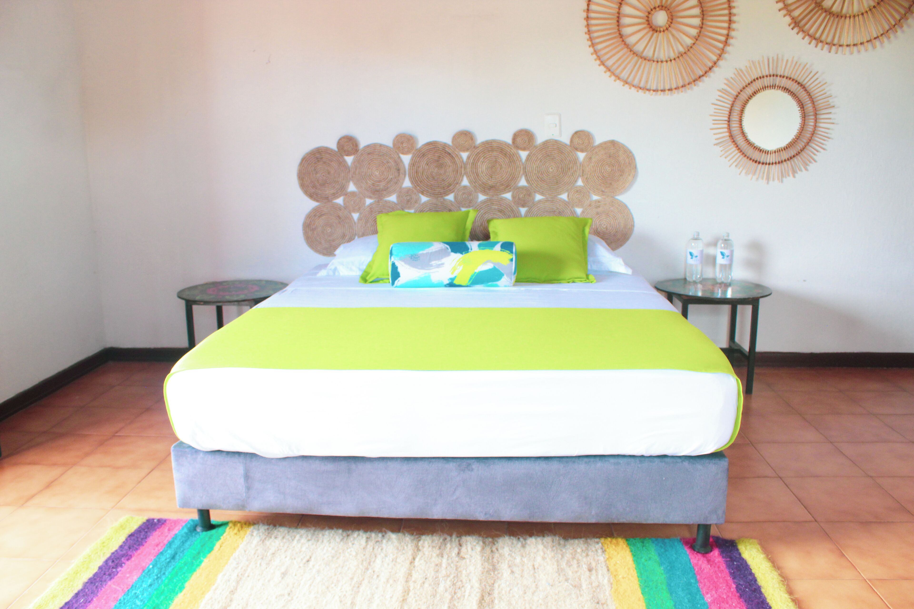 Un lit recouvert d’une couvre-lit verte et blanche, avec deux oreillers verts et un plaid bleu et blanc. Deux miroirs ronds sont accrochés au mur, au-dessus du lit.