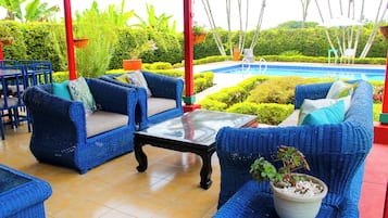 Zona de piscina con mobiliario de mimbre azul y una mesa de vidrio.