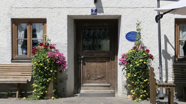 Un edificio con puerta de madera, un banco y arreglos florales.