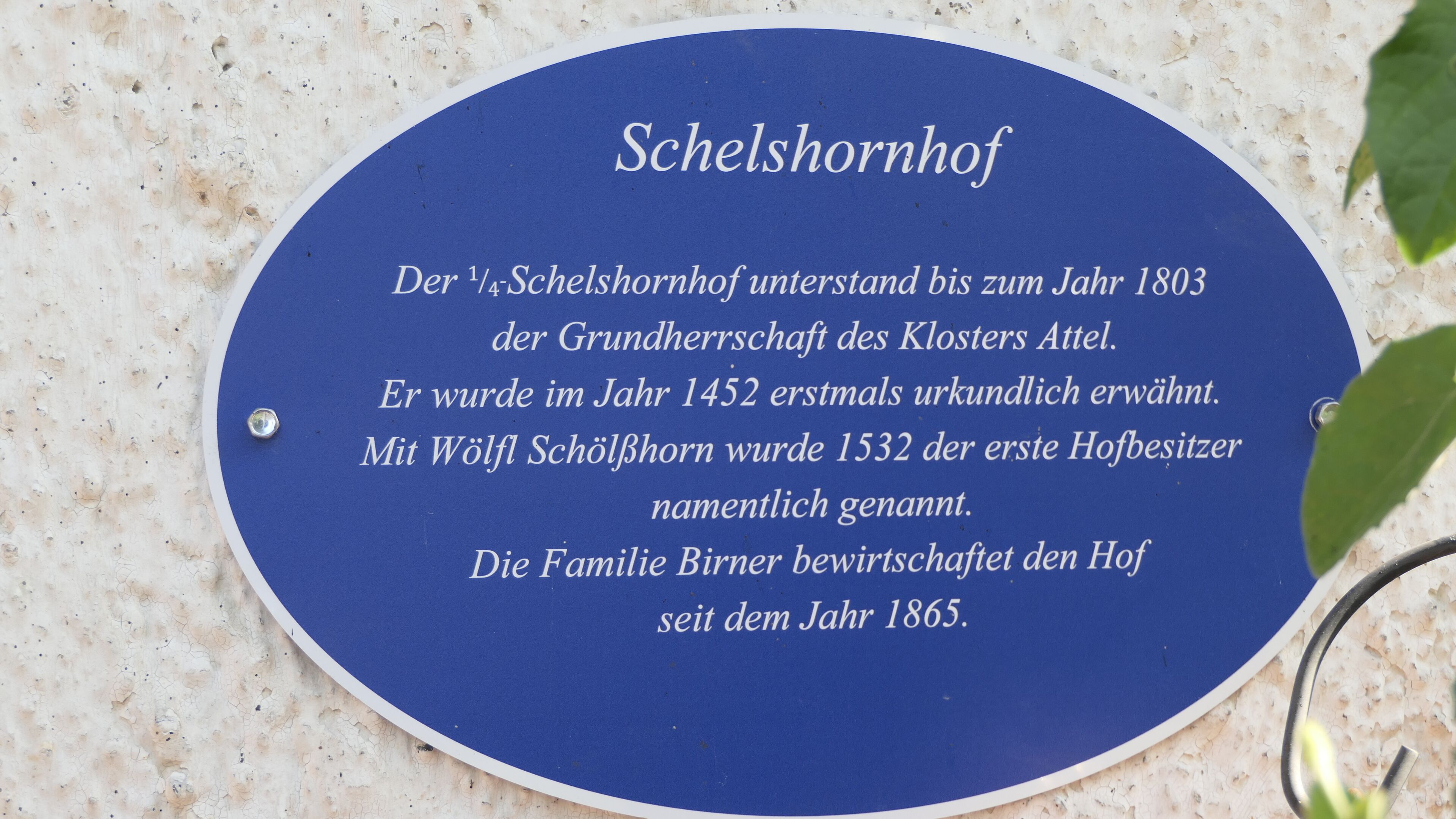 Eine blaue Tafel mit weißer Schrift auf einer strukturierten Wand.