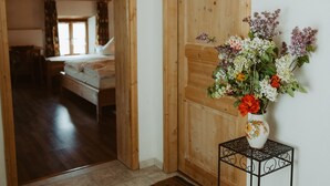 Una habitación con puerta de madera, una mesita con un florero y una cama con ventana.