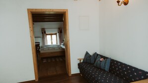 Una habitación con piso de madera, un sofá con cojines estampados, una cama con colcha a rayas y una ventana con cortinas.
