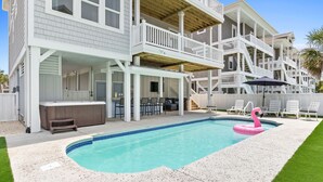 Ein zweistöckiges Haus mit überdachter Terrasse, Swimmingpool und einem Flamingo-Schwimmspielzeug.