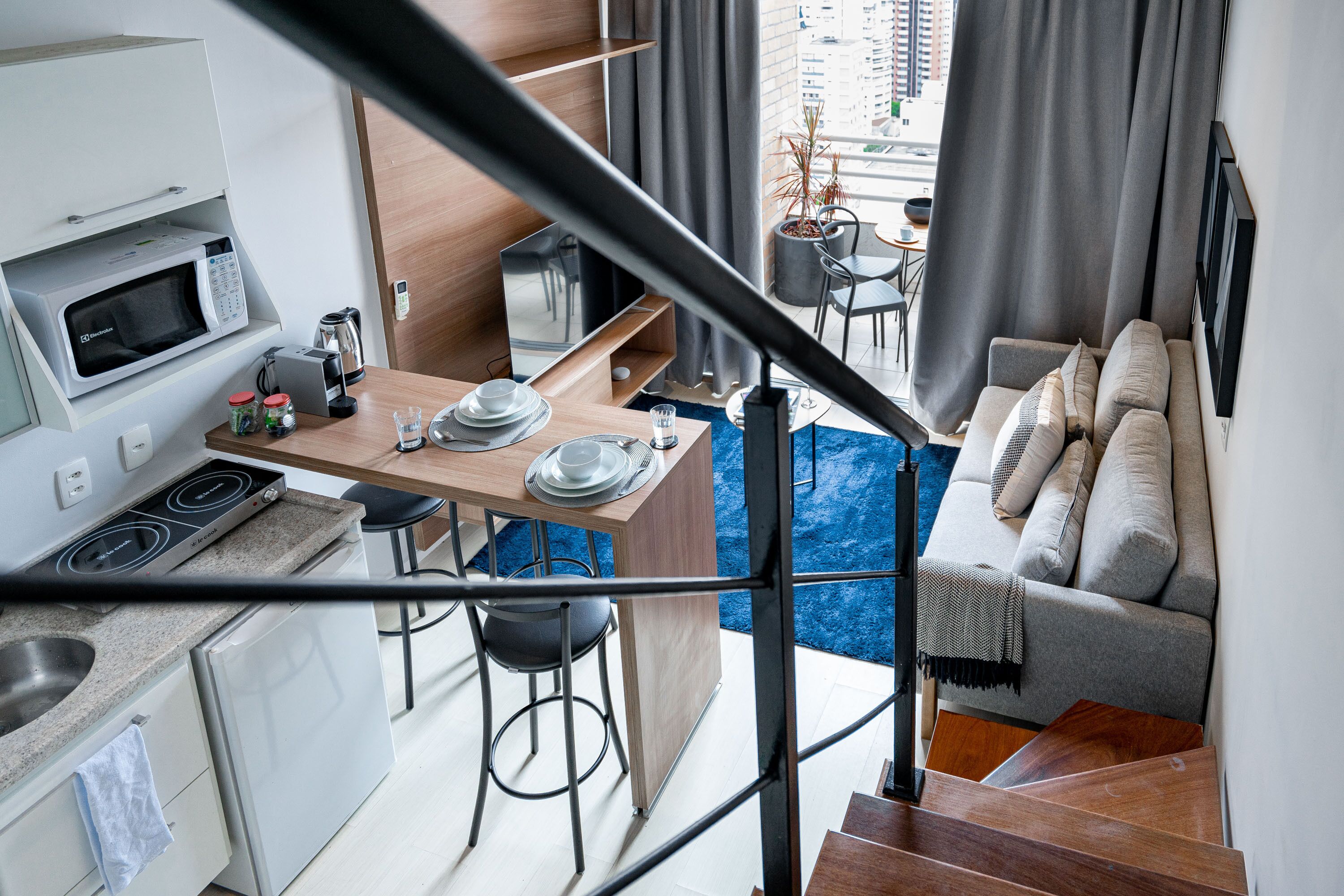 A modern kitchen with a microwave, stove, and sink, a dining area with a table and chairs, and a living area with a sofa and a view of the city.