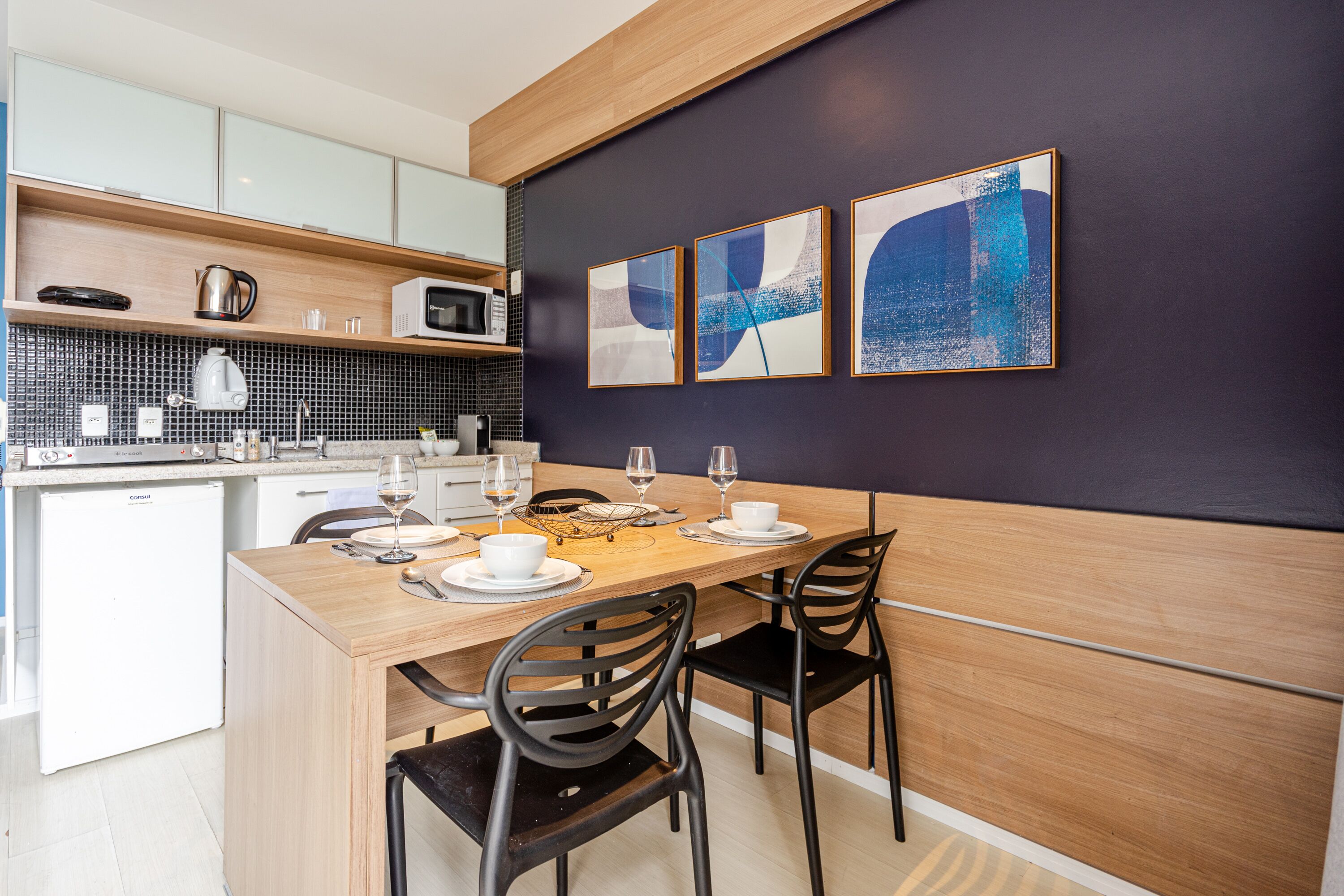 A modern kitchen with a wooden dining table set for four, equipped with black chairs.