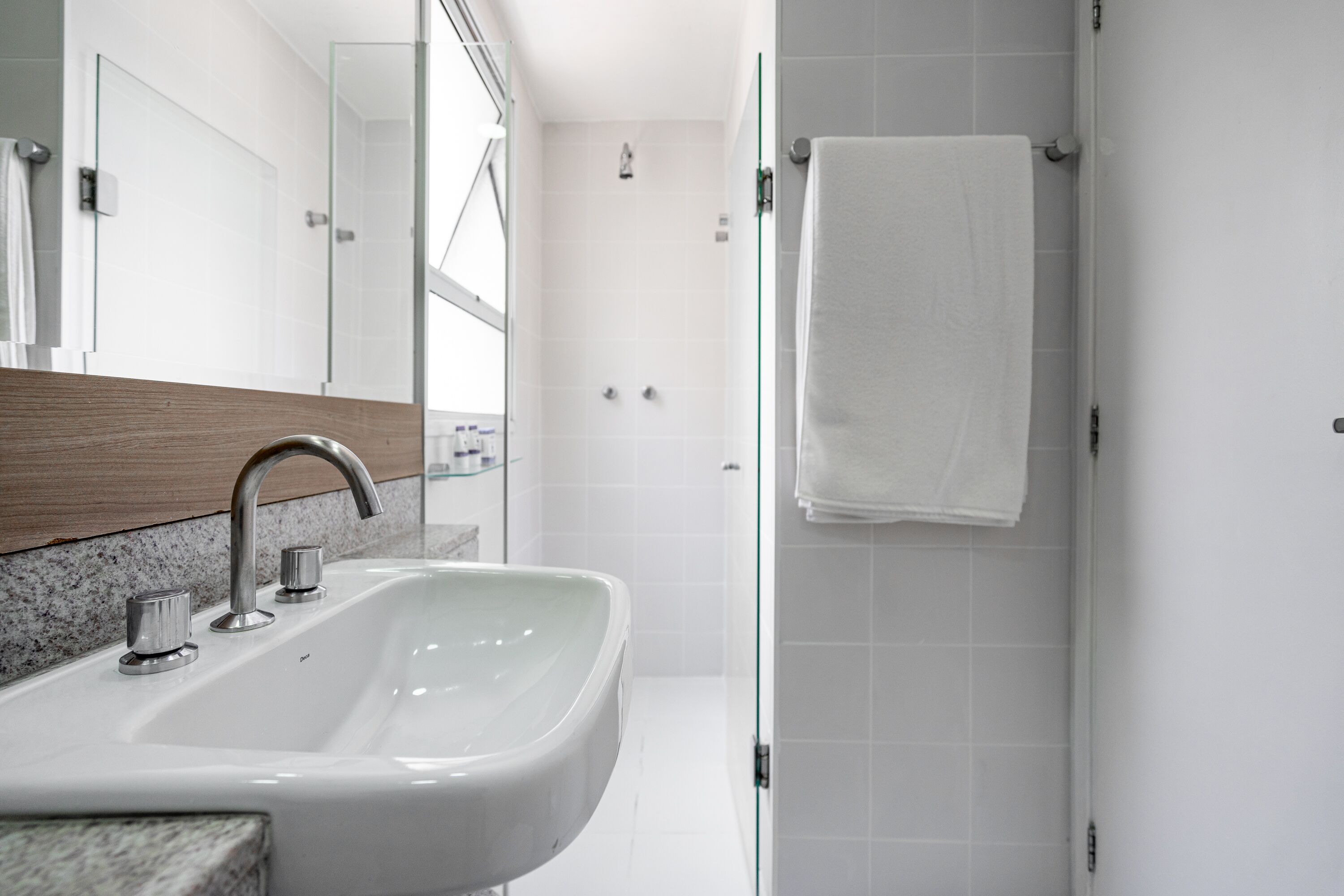 Un bagno moderno con lavandino bianco, un piano d'appoggio in legno e cabina doccia in vetro.