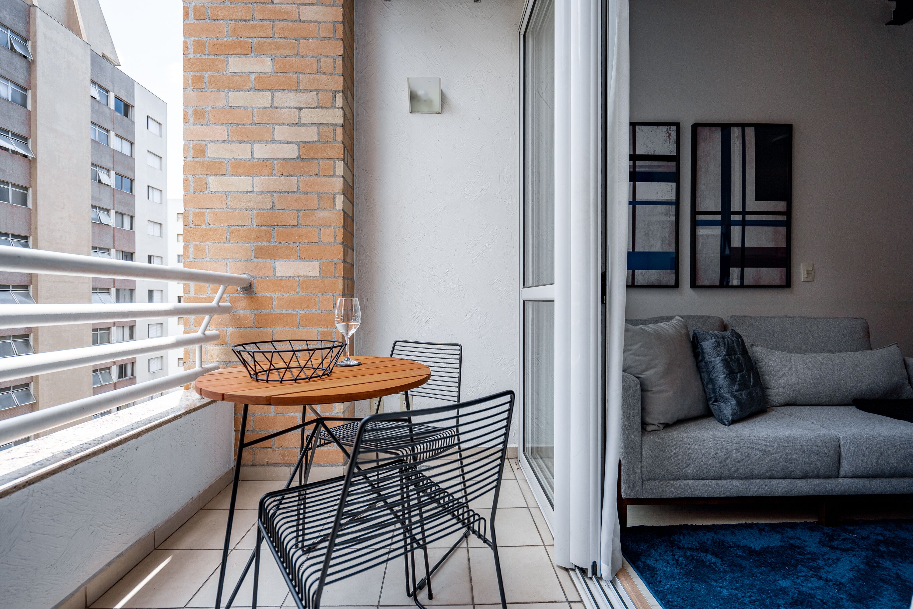 A balcony with a table and chairs, a grey sofa, and abstract wall art.