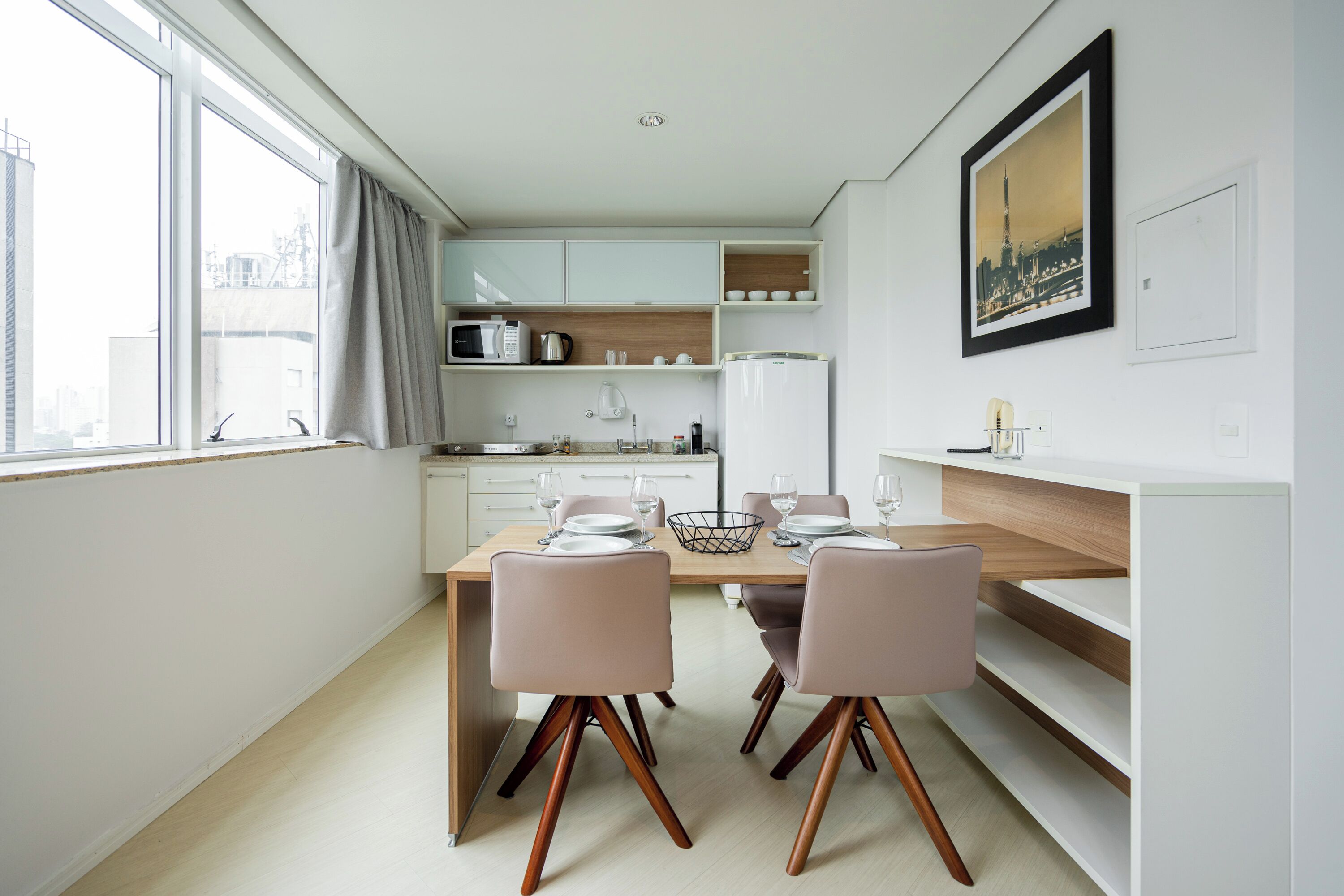 Une cuisine moderne avec des meubles blancs, une table à manger avec des chaises et une grande fenêtre avec des rideaux.