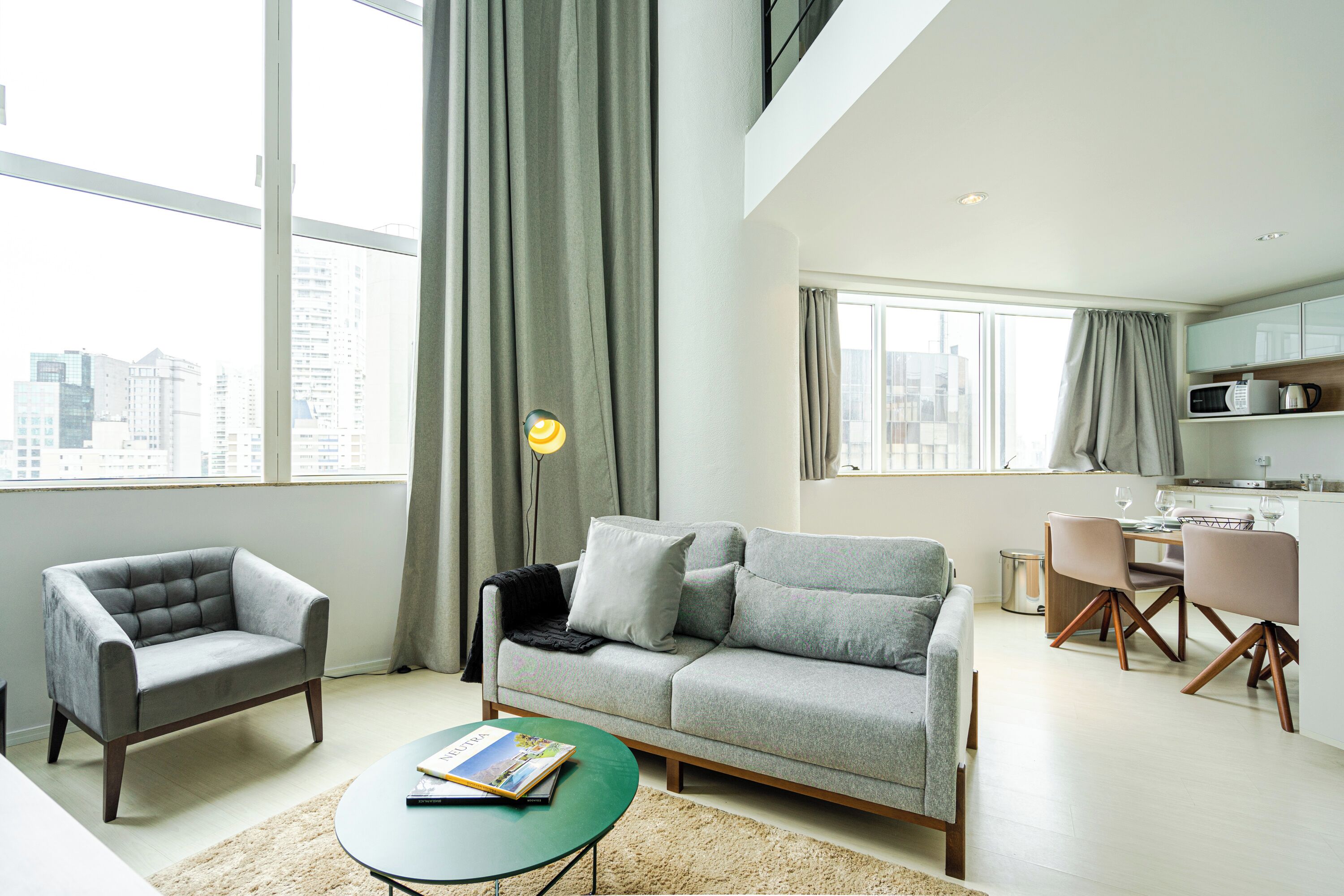 Ein modernes Wohnzimmer mit einem grauen Sofa, einem passenden Sessel, einem grünen Couchtisch und einem Essbereich mit Tisch und Stühlen.