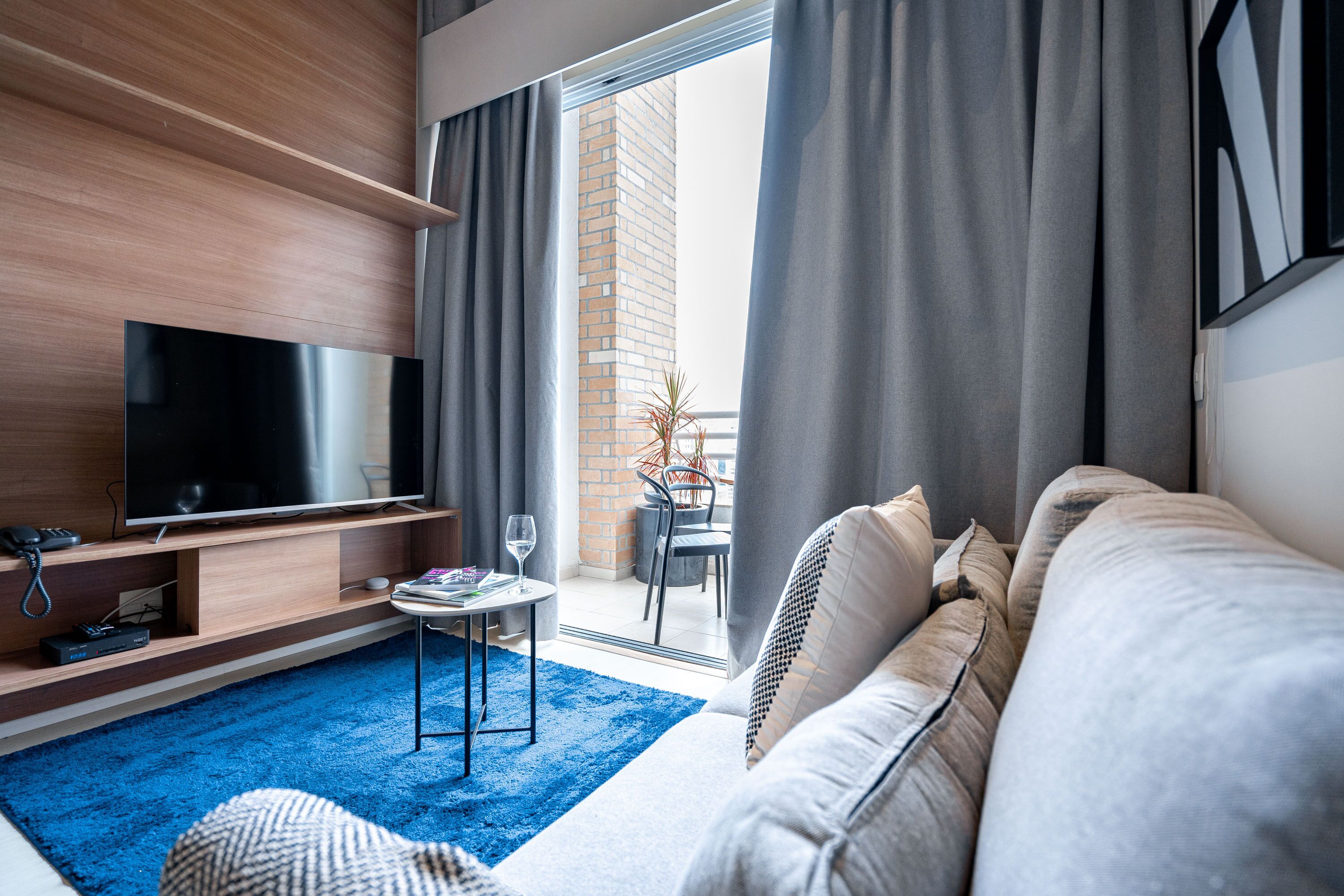 A modern living room with a flat-screen TV, a sofa, a coffee table, and a blue carpet.