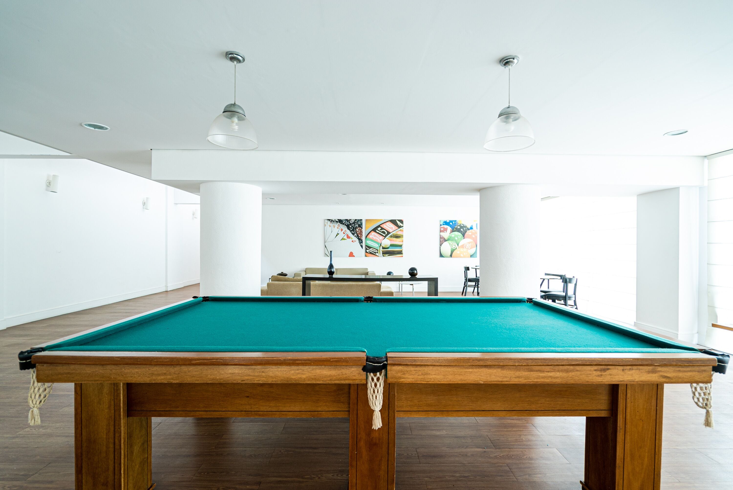 A pool table in a well-lit room with white walls and a wooden floor.