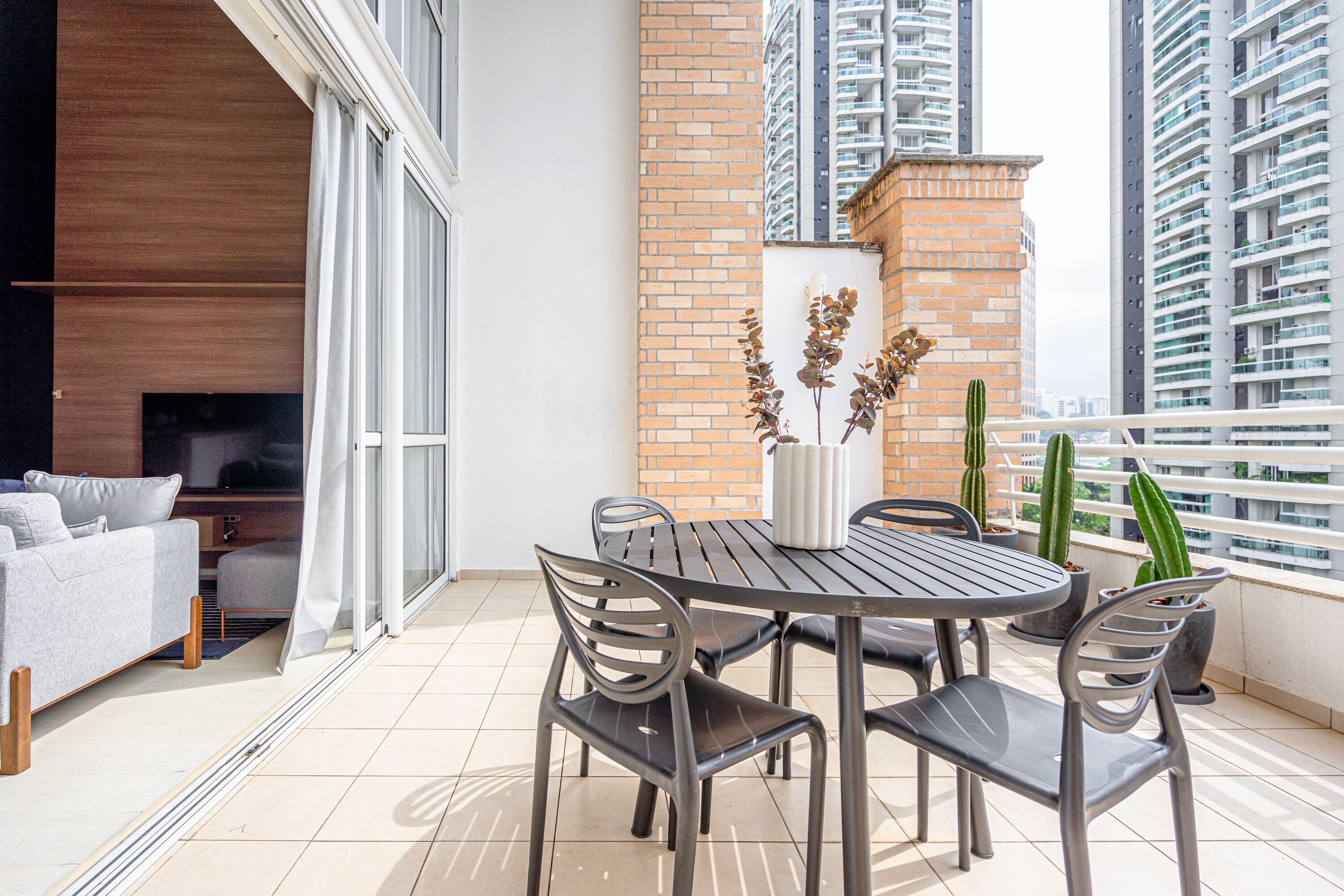 A modern balcony with a dining table, chairs, and potted plants.