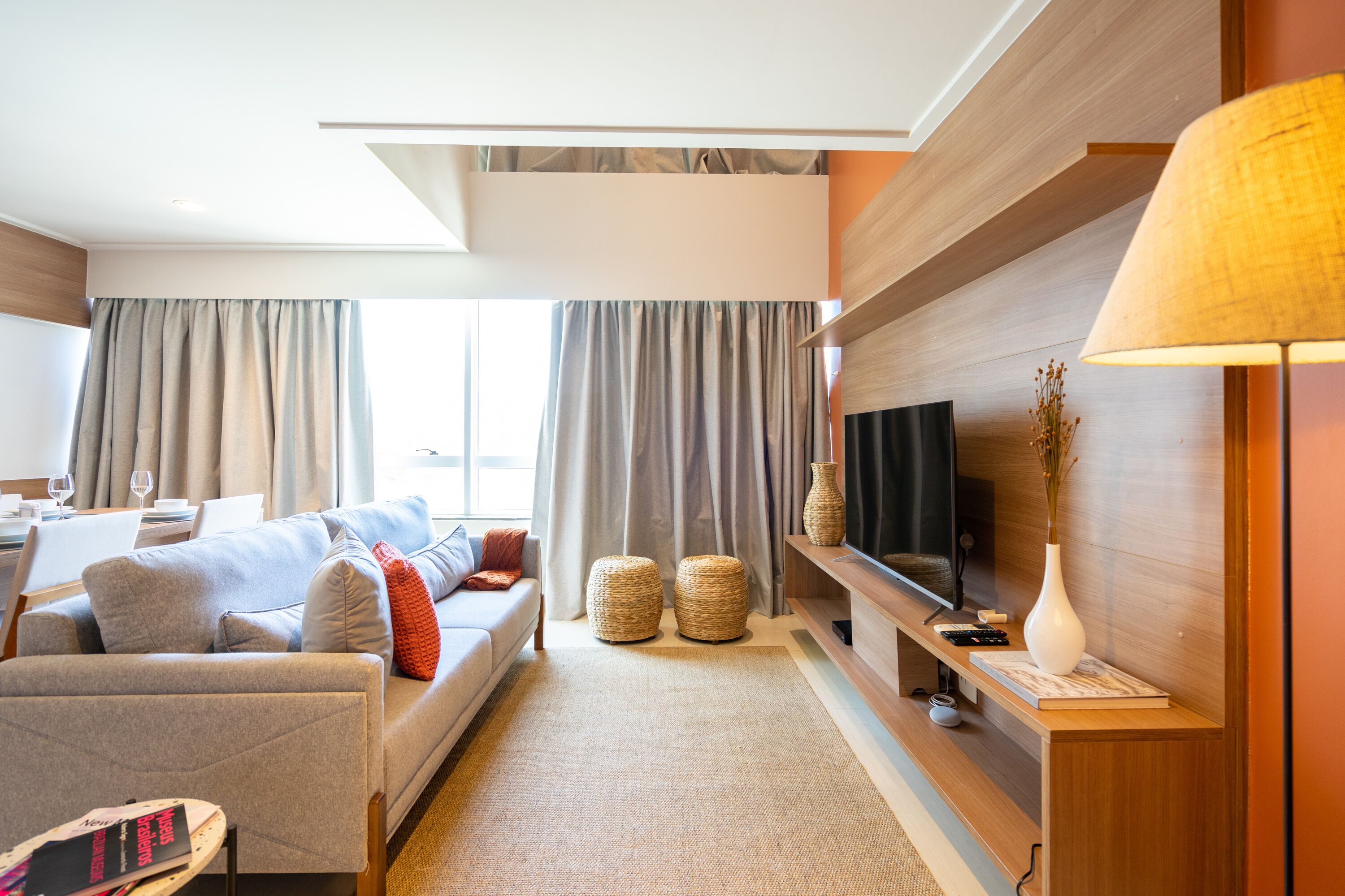 A modern living room with a sofa, ottomans, a flat-screen TV, and a lamp.