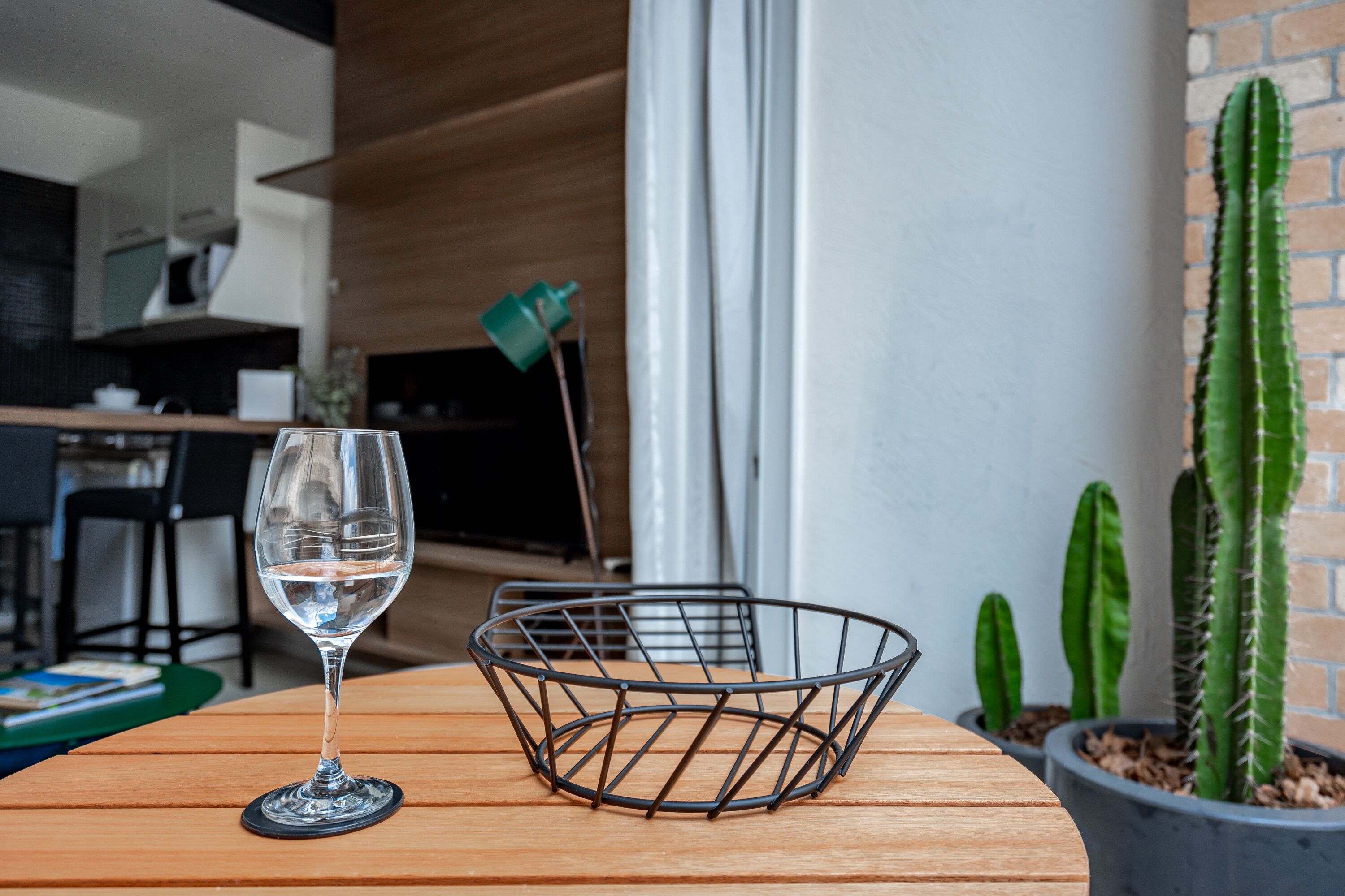 Un verre d’eau sur une table en bois, avec un panier en fil de fer, une plante succulente et, au fond, une cuisine moderne.