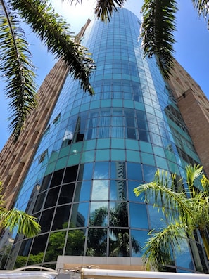 A tall, modern glass building with a reflective facade, surrounded by palm trees.