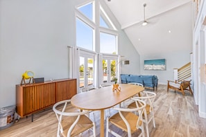 A spacious room with a wooden dining table, white chairs, a blue sofa, and a staircase. - The Hammock House: Bright and modern pool home with outdoor living space (Anna Maria)
