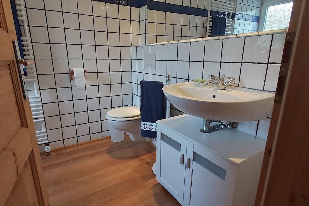 Ett badrum med vita kakelbeklädda väggar, en vit handfat och en toalett.