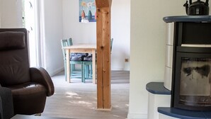 Una habitación con un sillón de cuero marrón, una mesa de comedor de madera con sillas y un estufa de leña.