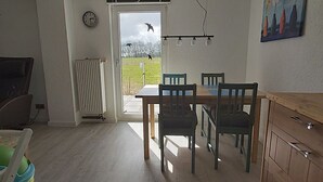 Un comedor con una mesa, sillas, un radiador, un reloj y vistas a un jardín con pájaros.