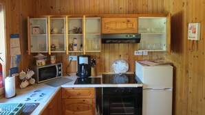A wooden-paneled kitchen with a microwave, coffee maker, and a refrigerator. There are cabinets with glass doors, a sink, and a fire blanket sign on the wall. - Oak Lodge Cosy Cabin With 2 Bedrooms. Open all year. 15 miles from Fort William (Roybridge)