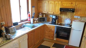 A compact kitchen with wooden cabinets, a washing machine, a microwave, and a refrigerator. - Oak Lodge Cosy Cabin With 2 Bedrooms. Open all year. 15 miles from Fort William (Roybridge)