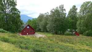 A red barn in a grassy field with trees and a mountain in the background. - Oak Lodge Cosy Cabin With 2 Bedrooms. Open all year. 15 miles from Fort William (Roybridge)