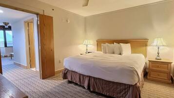 A hotel room with a large bed, two bedside tables with lamps, a ceiling fan, and a carpeted floor.