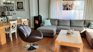 A cozy living room with a sofa, a coffee table, a leather chair, a dining table with chairs, a kitchen area, and a wood-burning stove. - 6p Luxury apartment with panoramic roof terrace (Burgerbrug)