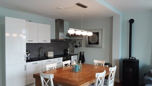 A modern kitchen with white cabinets, a wooden dining table, and a black wood-burning stove. - 6p Luxury apartment with panoramic roof terrace (Burgerbrug)